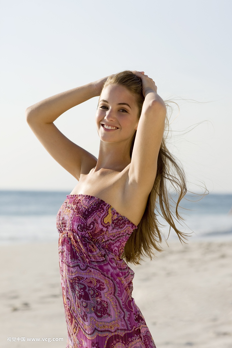 快乐的金发女人在海滩上的紫色夏季连衣裙