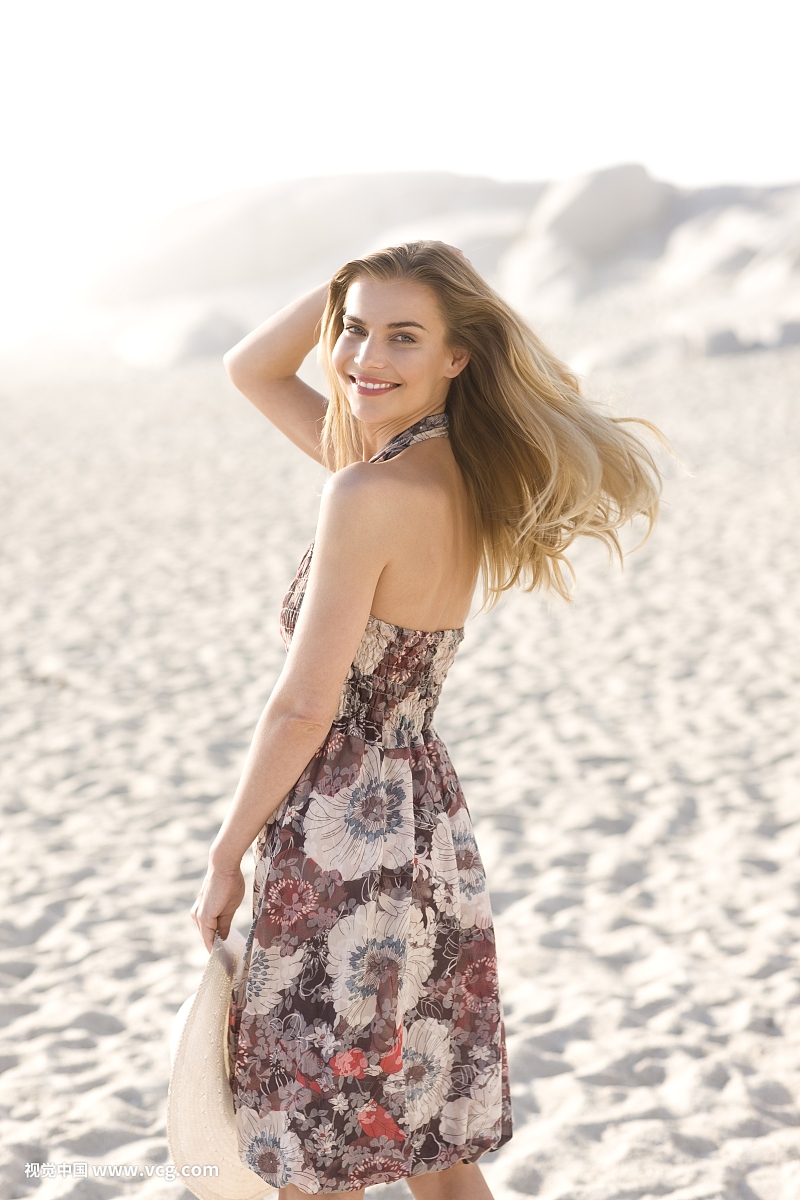 年轻的金发女人在海滩上的一件花礼服