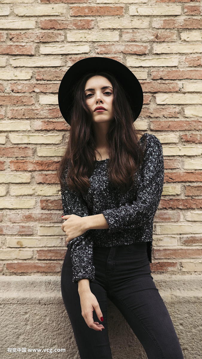 Fashionable young woman wearing black hat standing in front of facade