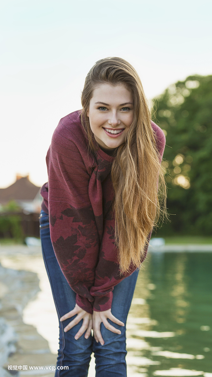 Portrait of cheerful young woman with long hair standing by lake