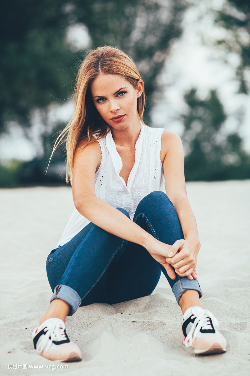 Young woman sitting on the beach sand and posing