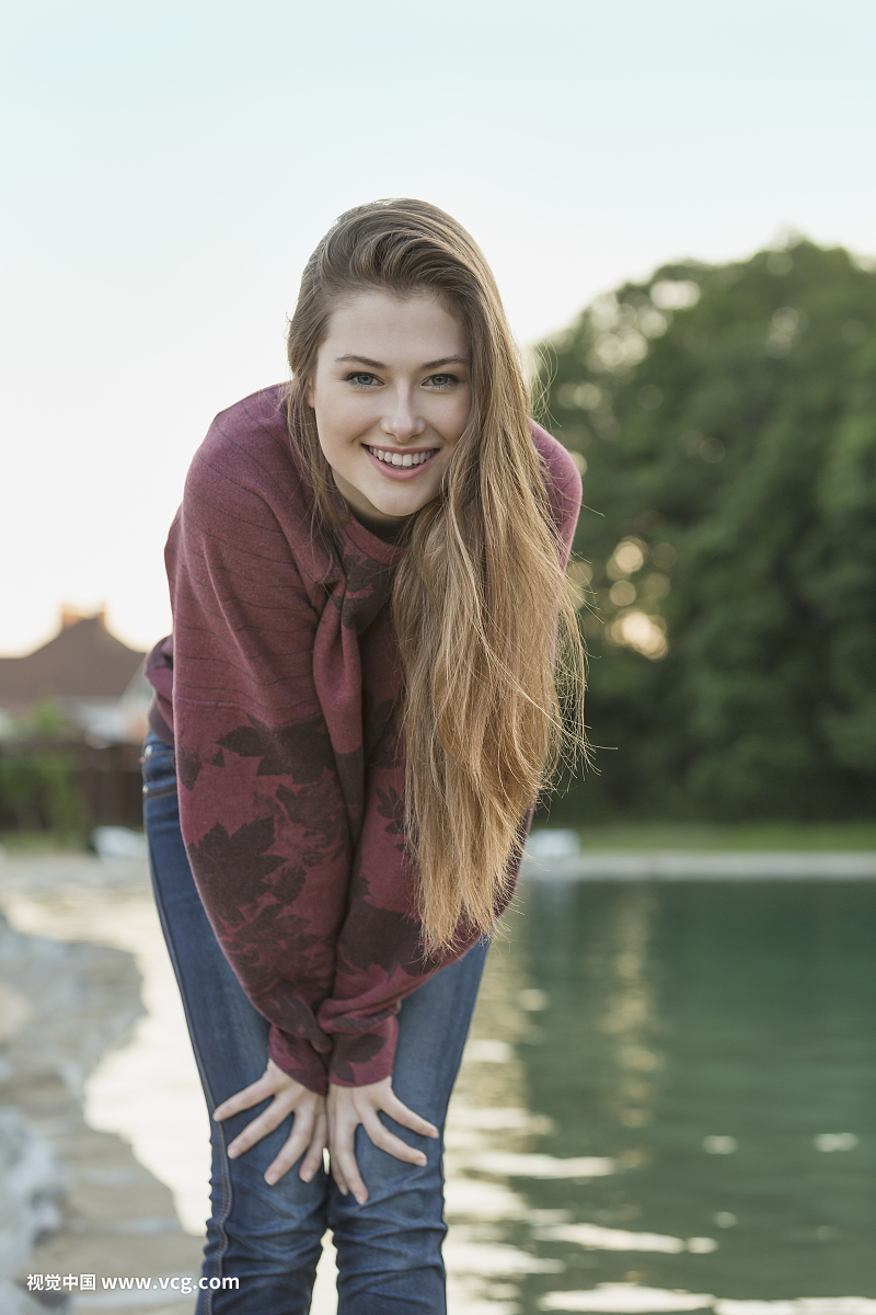 Portrait of cheerful young woman with long hair standing by lake