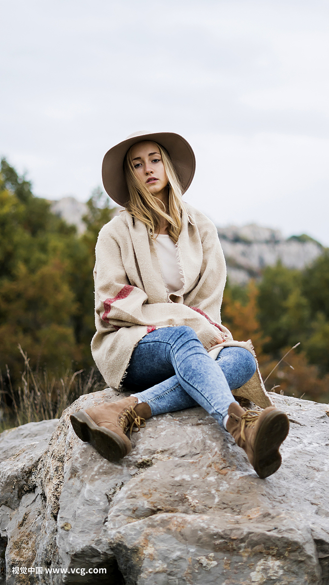 Young woman wearing hat sitting on boulder