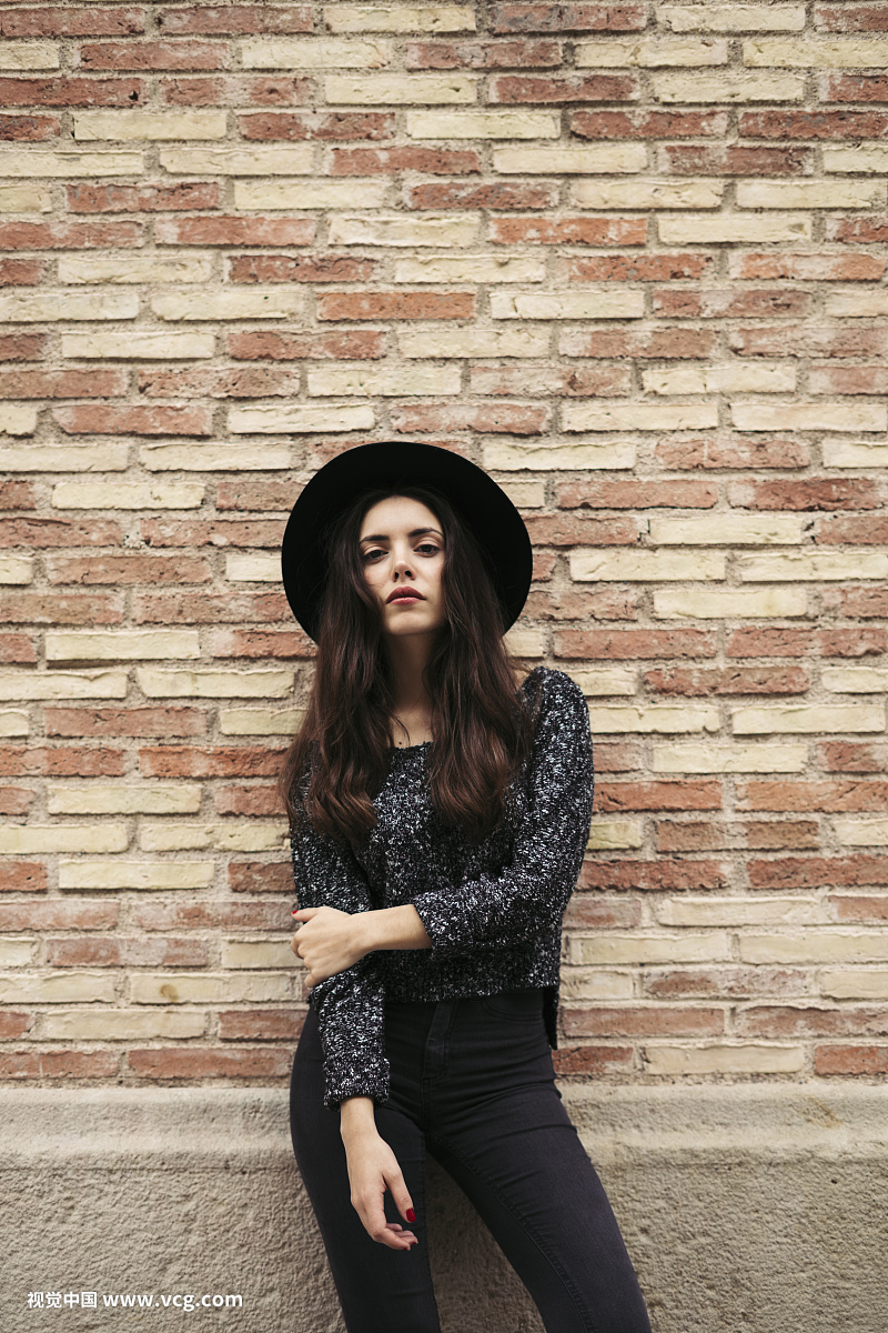 Fashionable young woman wearing black hat standing in front of facade