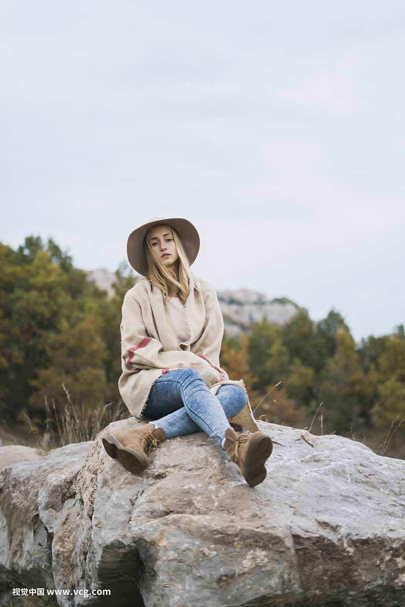 Young woman wearing hat sitting on boulder
